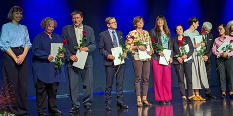 Powiększ grafikę: Wyróżnieni nauczyciele stoją na scenie. Trzymają dyplomy i kwiaty.