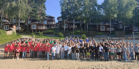 Powiększ grafikę: Duża grupa uczniów na plaży. W tle domki letniskowe.